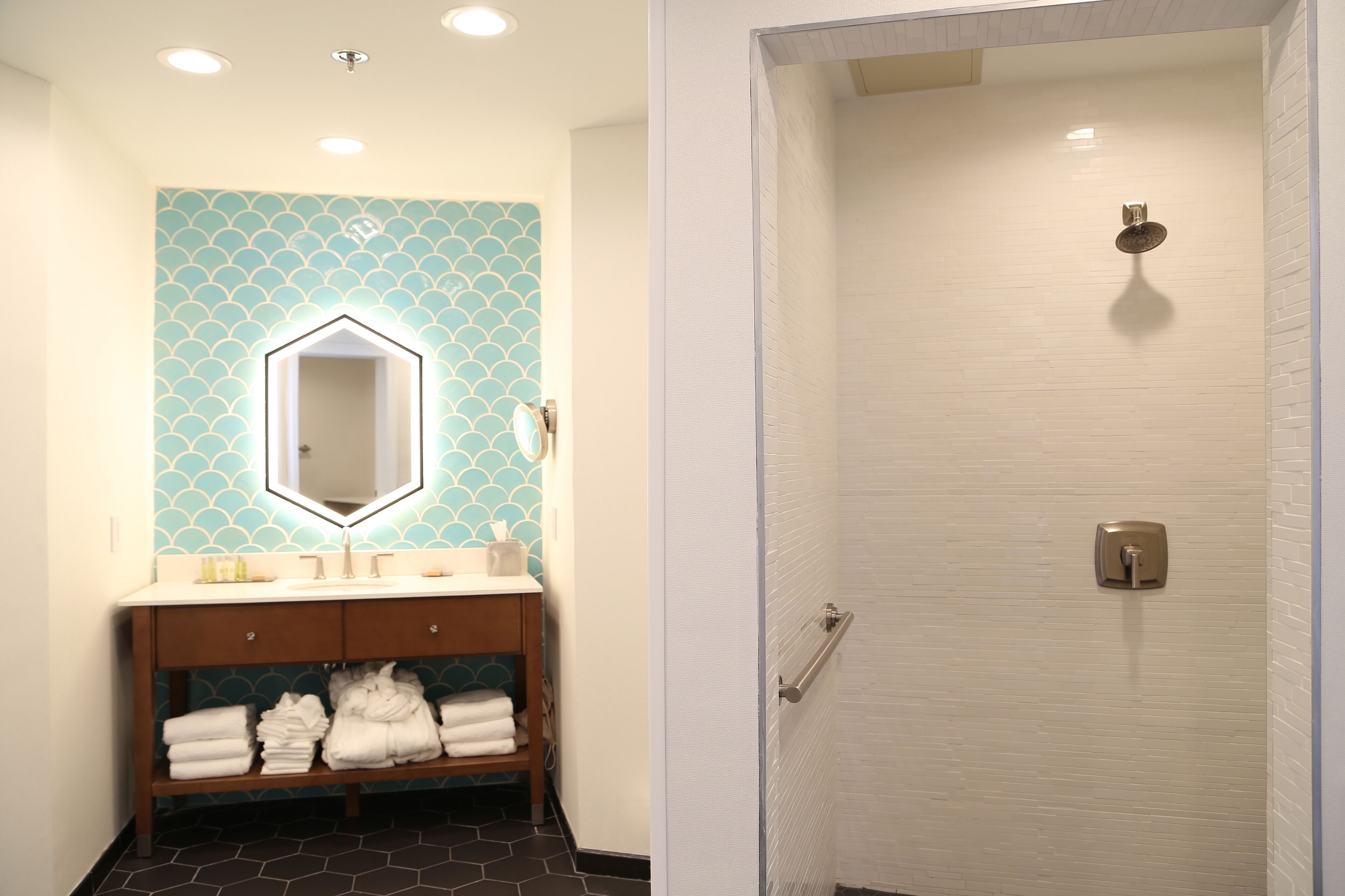A bathroom with a tiled wall, a sink with a mirror, and a shower area.