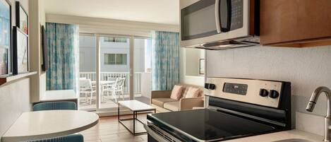 A modern kitchen with a built-in microwave, stove, and sink. There is a dining area with a table and chairs, and a balcony with a view.