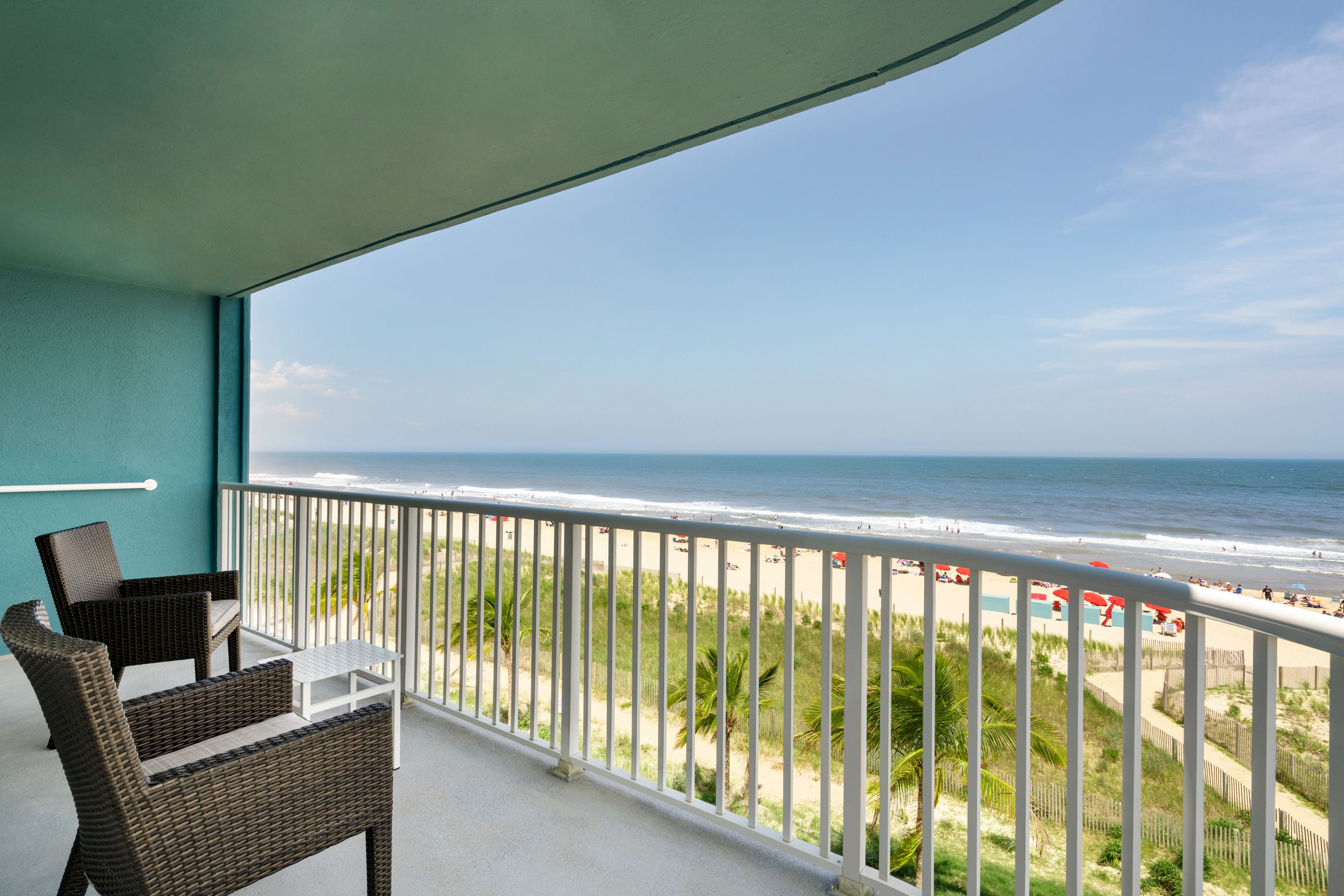 A balcony with wicker furniture overlooking a beach.
