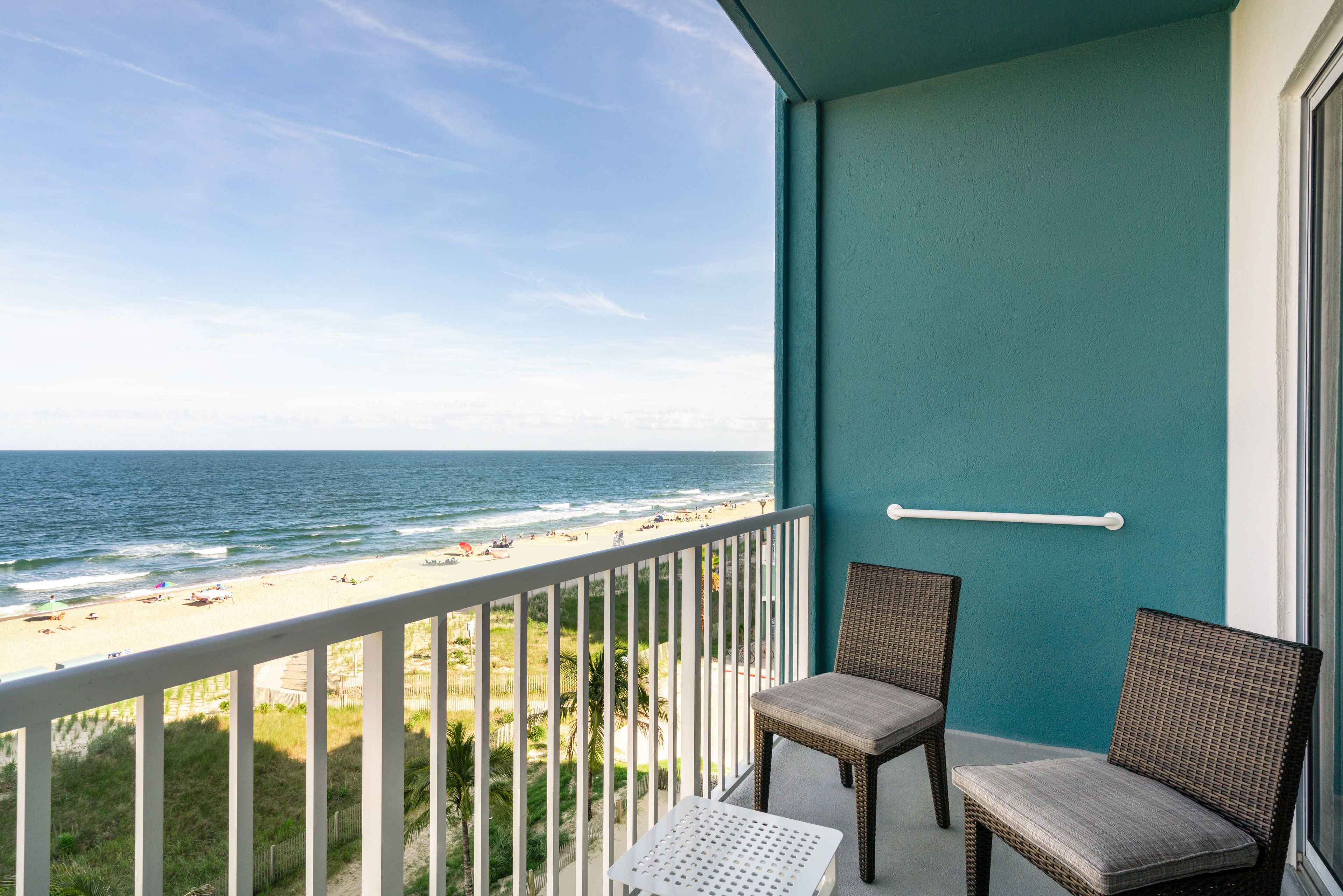 A balcony with a view of the beach, two wicker chairs, and a small table.