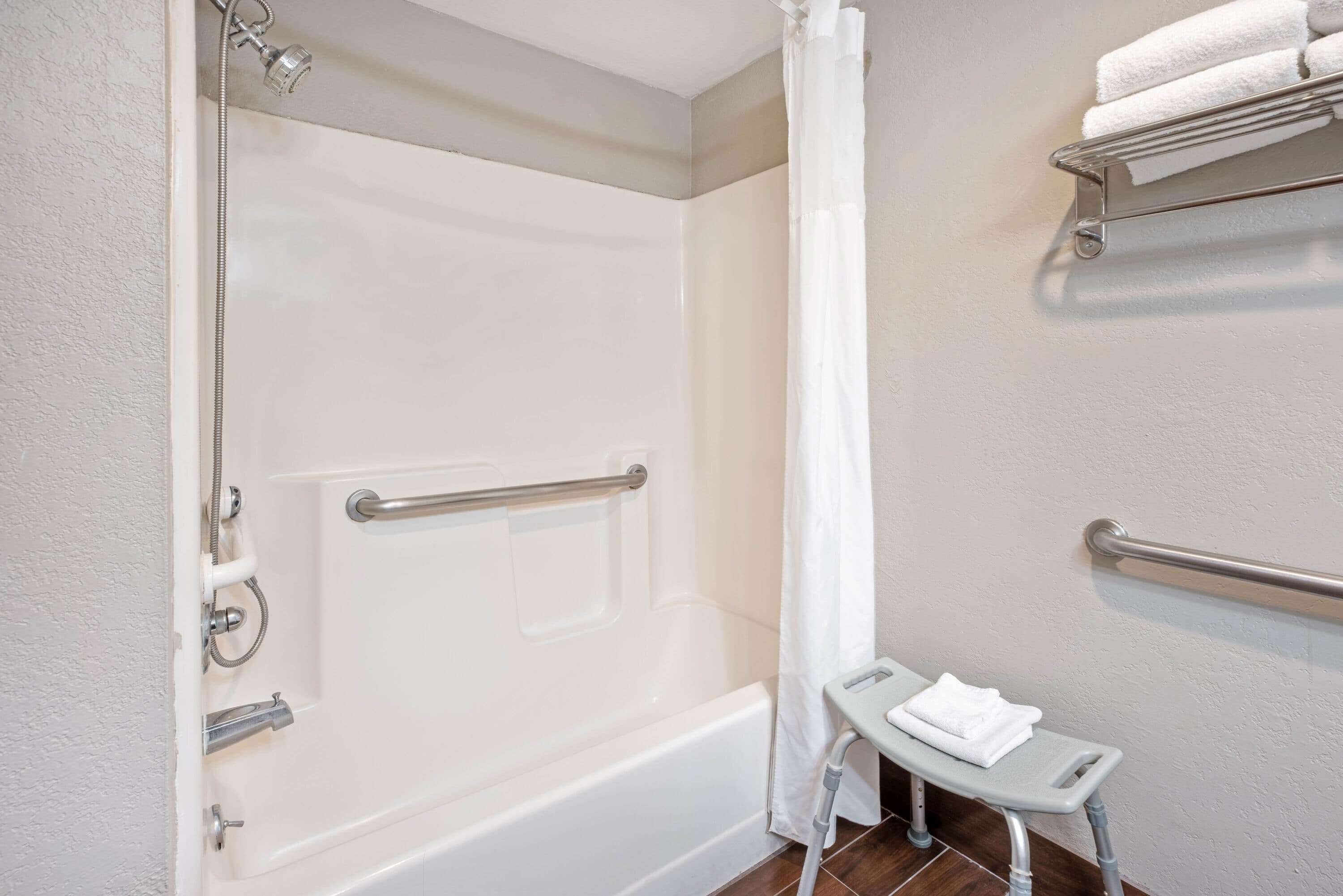 Une salle de bain équipée d’une baignoire, d’une douche, d’une barre d’appui, d’un porte-serviettes et d’un petit tabouret.