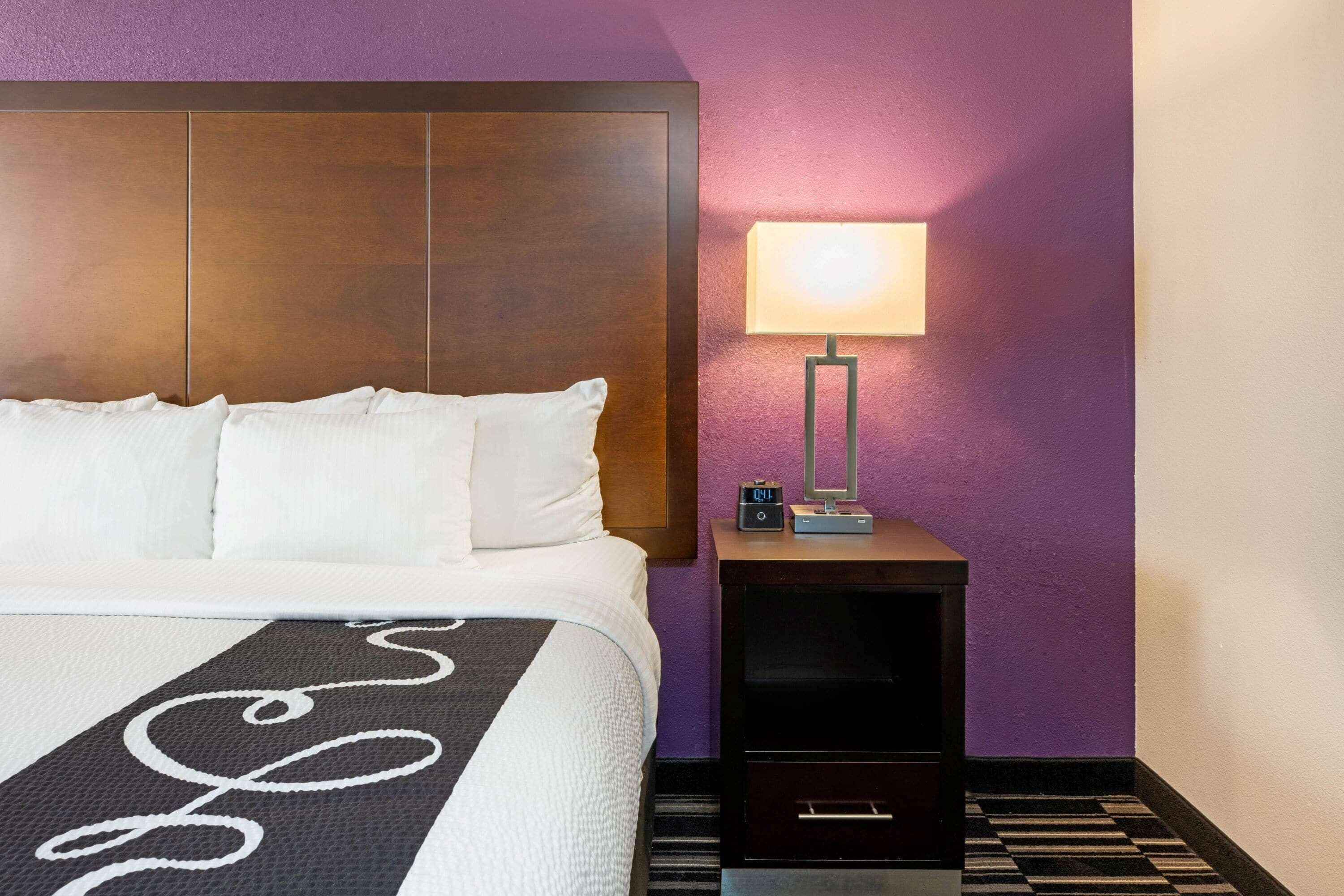 A hotel room with a large bed, a nightstand with a lamp, and a digital clock.