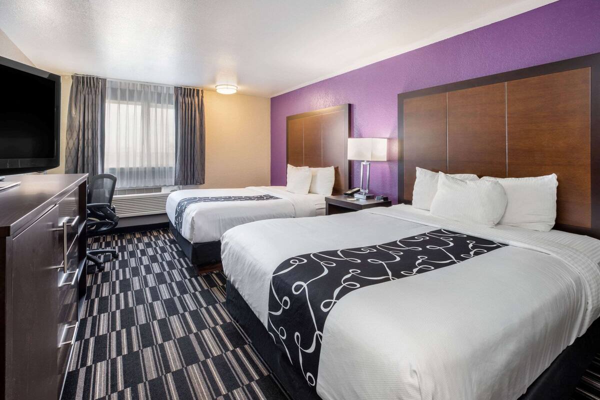 A hotel room with two beds, a desk, a TV, and a window with curtains.