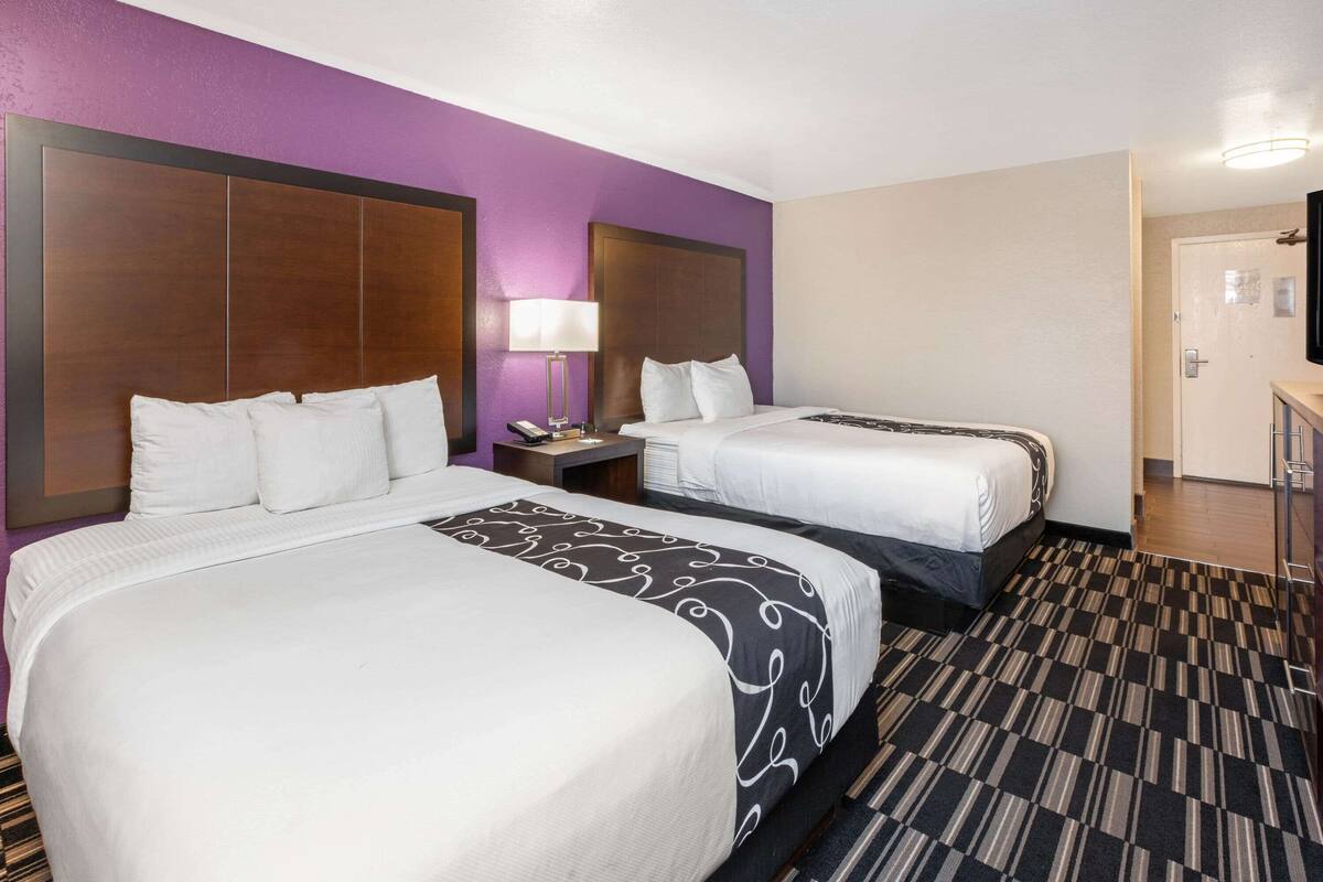 A hotel room with two beds, a nightstand with a lamp, and a bathroom door.