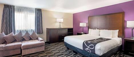 A hotel room with a bed, a sofa, a desk, and a wardrobe.
