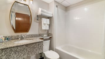 A bathroom with a granite countertop sink, a toilet, a bathtub, and a mirror with lights.