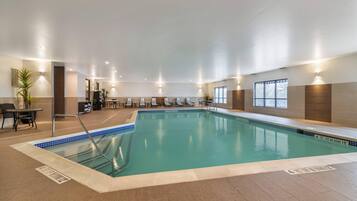 An indoor swimming pool with a tiled edge, a pool ladder, and a seating area with tables and chairs.
