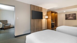 Une chambre d’hôtel avec deux lits, un téléviseur à écran plat fixé au mur, une armoire en bois et un tableau accroché au mur.