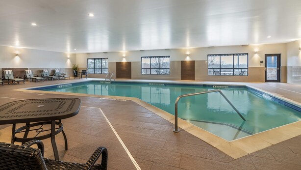 Une piscine intérieure à l’eau claire, entourée de chaises longues et d’une table.