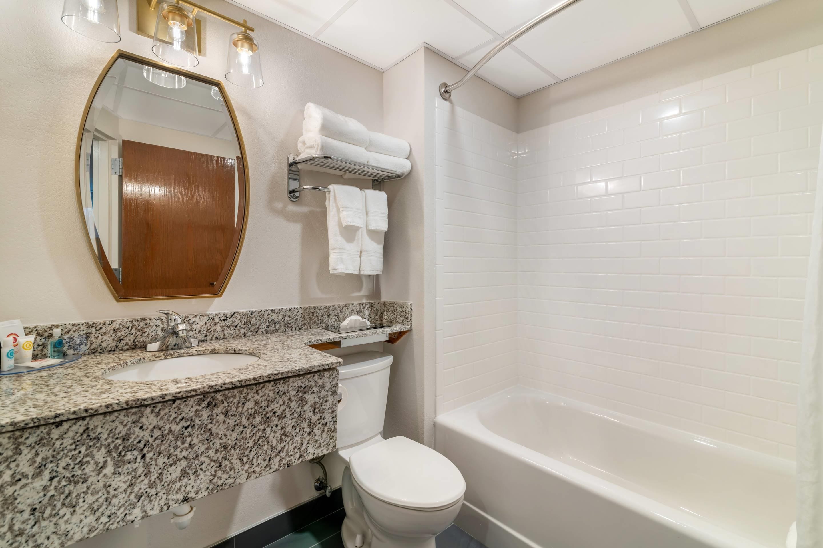 A bathroom with a granite countertop sink, a toilet, a bathtub, and a mirror with three lights.