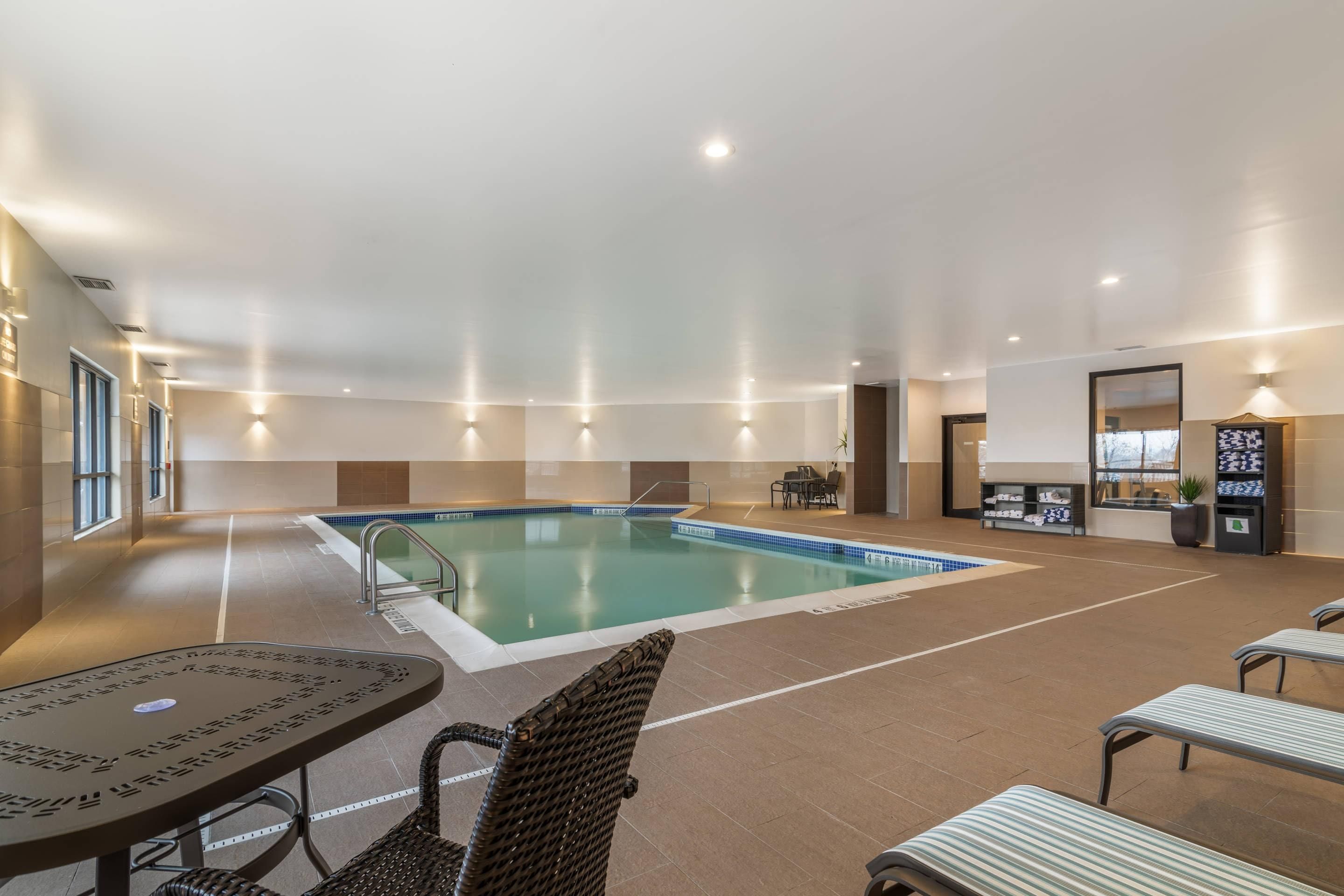 An indoor swimming pool area with a lounge area, seating, and a small bar.