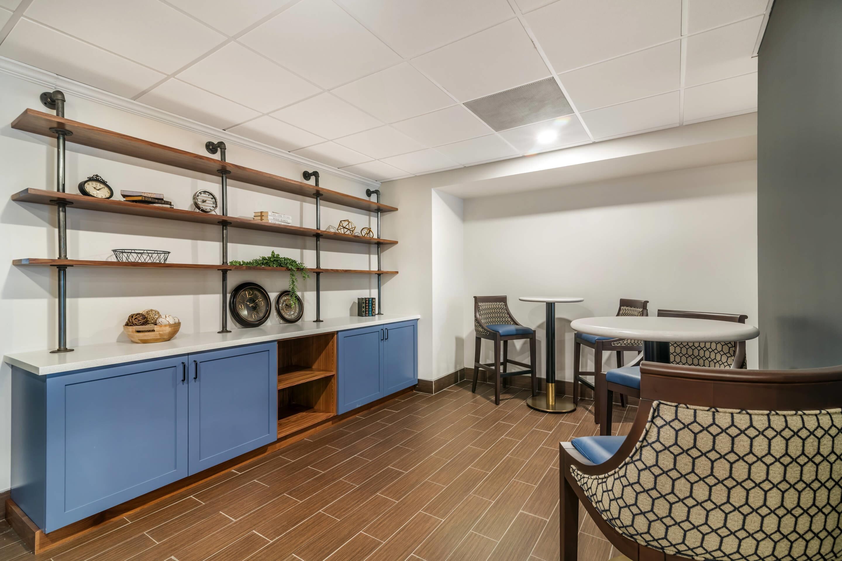 A modern kitchen with blue cabinets, wooden shelves, and a dining area with a round table and chairs.