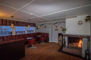 A cozy interior with a fireplace, seating area, and a view through large windows. - Lakselv Hotel (Porsanger)