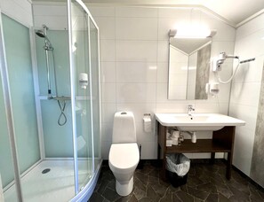 A bathroom with a glass-enclosed shower, a toilet, a sink, and a mirror. - Lakselv Hotel (Porsanger)