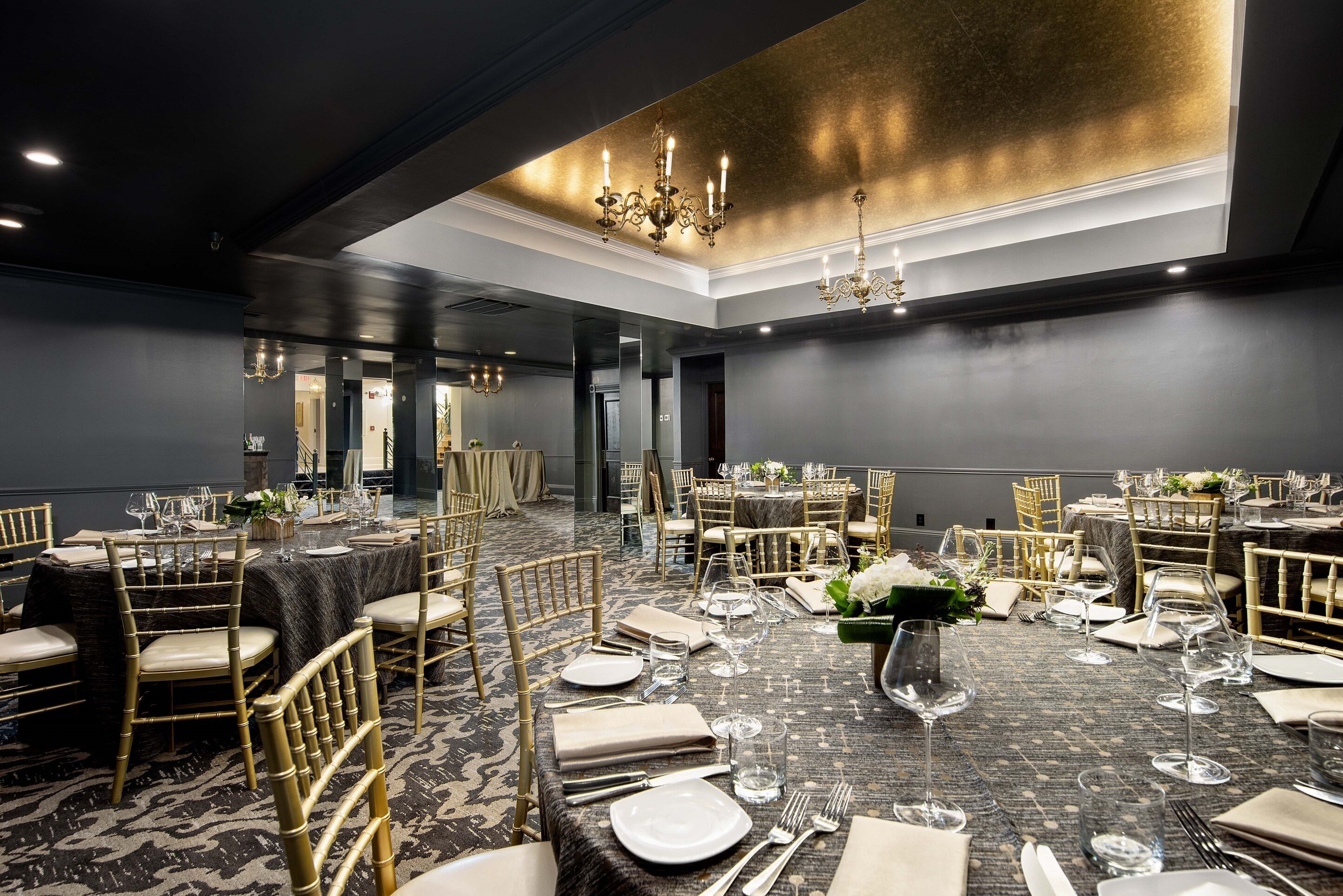 Une salle de banquet avec des tables rondes dressées pour le repas, des chaises dorées et des lustres.