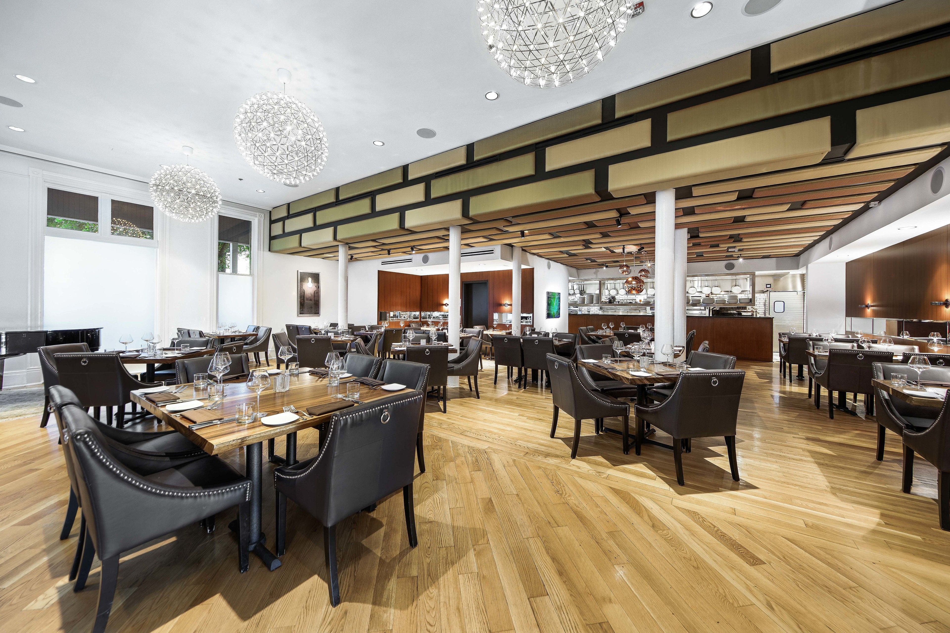 A spacious restaurant with high ceilings, wooden flooring, and modern chandeliers.