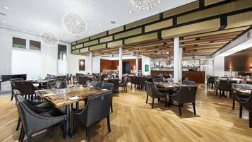 A spacious restaurant with high ceilings, wooden flooring, and modern chandeliers.