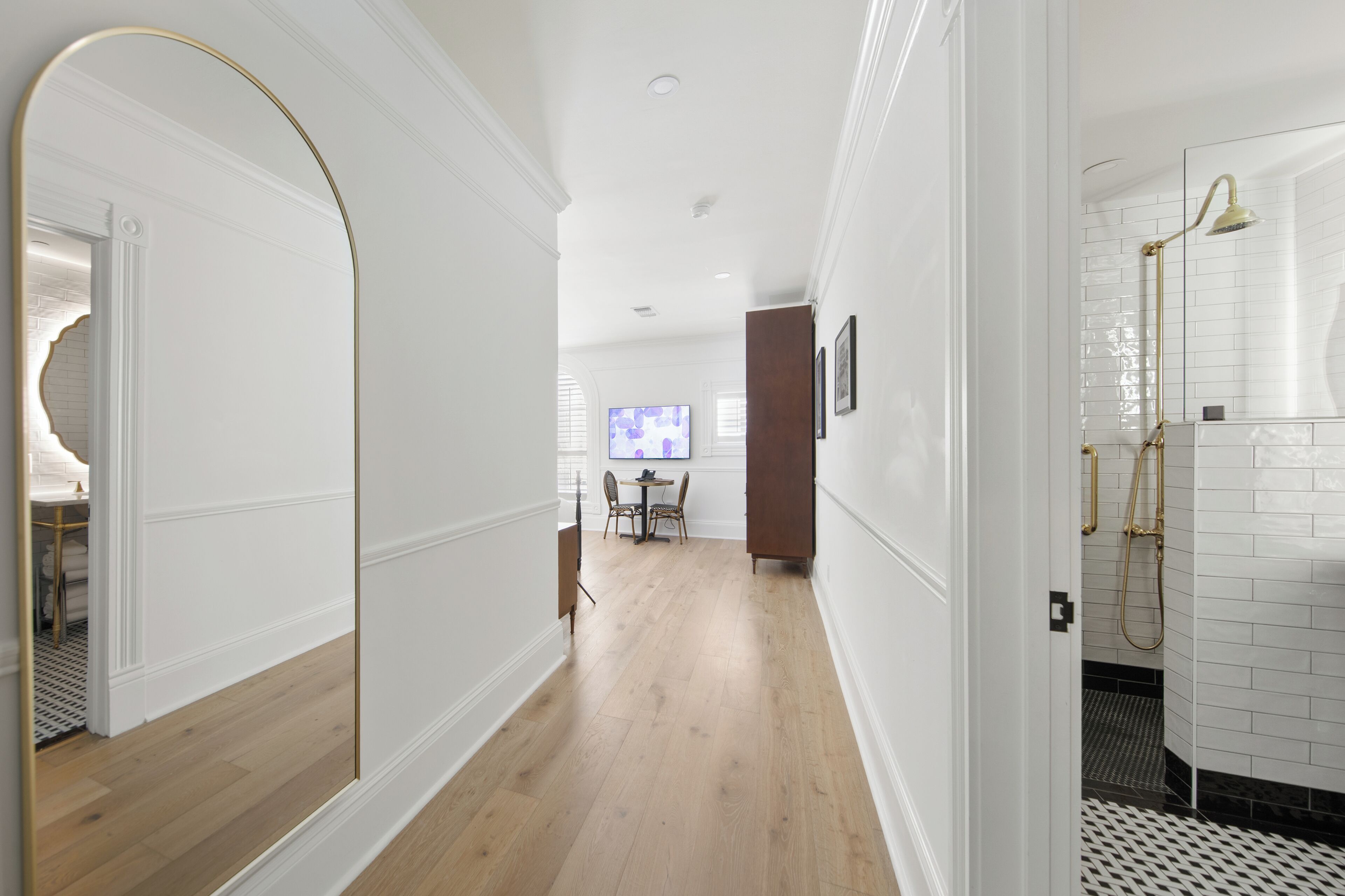 Käytävän lattia on puuta, seinät ovat valkoiset, ja vasemmalla puolella on peiliseinä. Taustalla näkyy ruokailutila, jossa on pöytä ja tuolit.