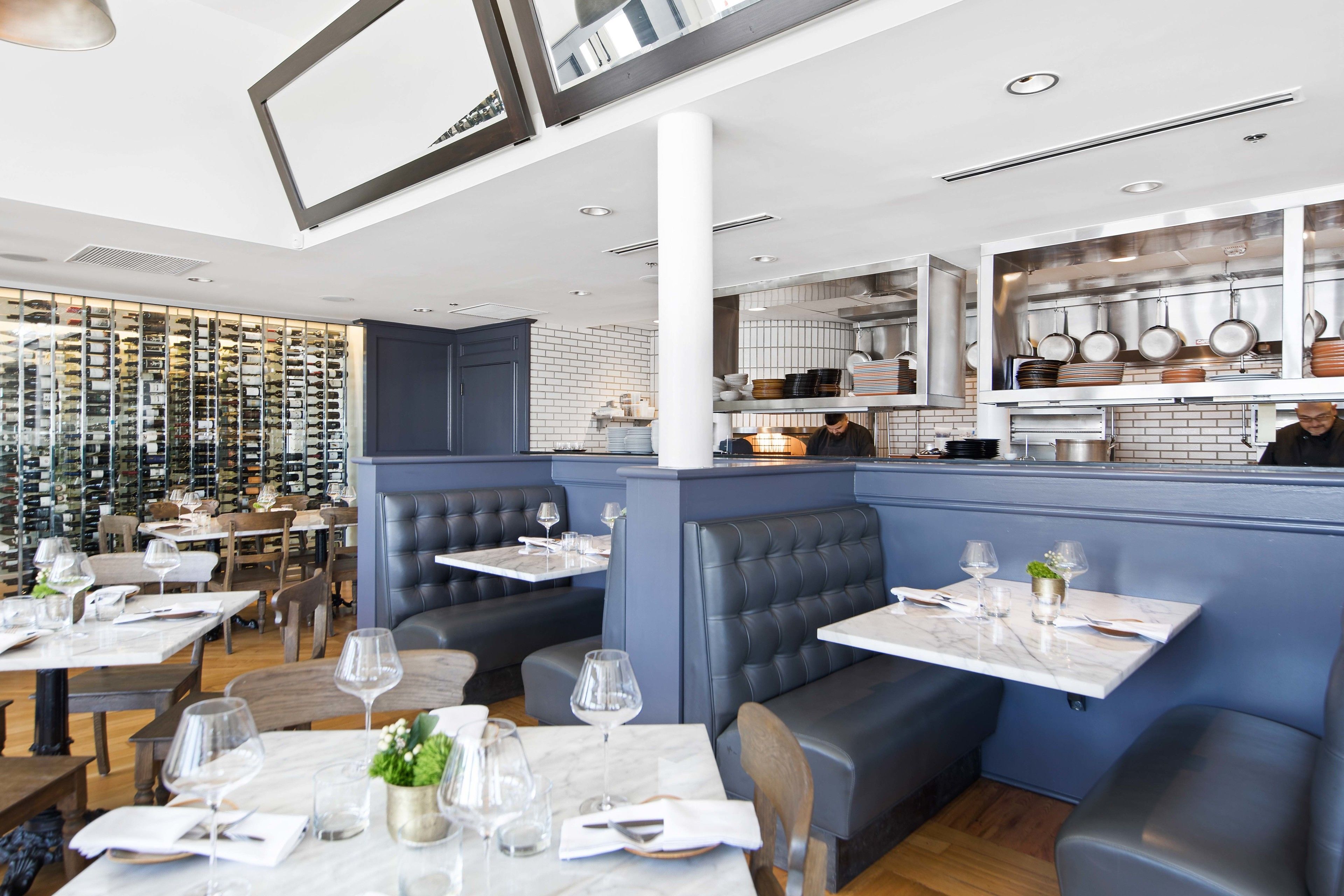 Un restaurant amb taules de marbre, seients de color blau fosc i una prestatgeria de vi al fons.