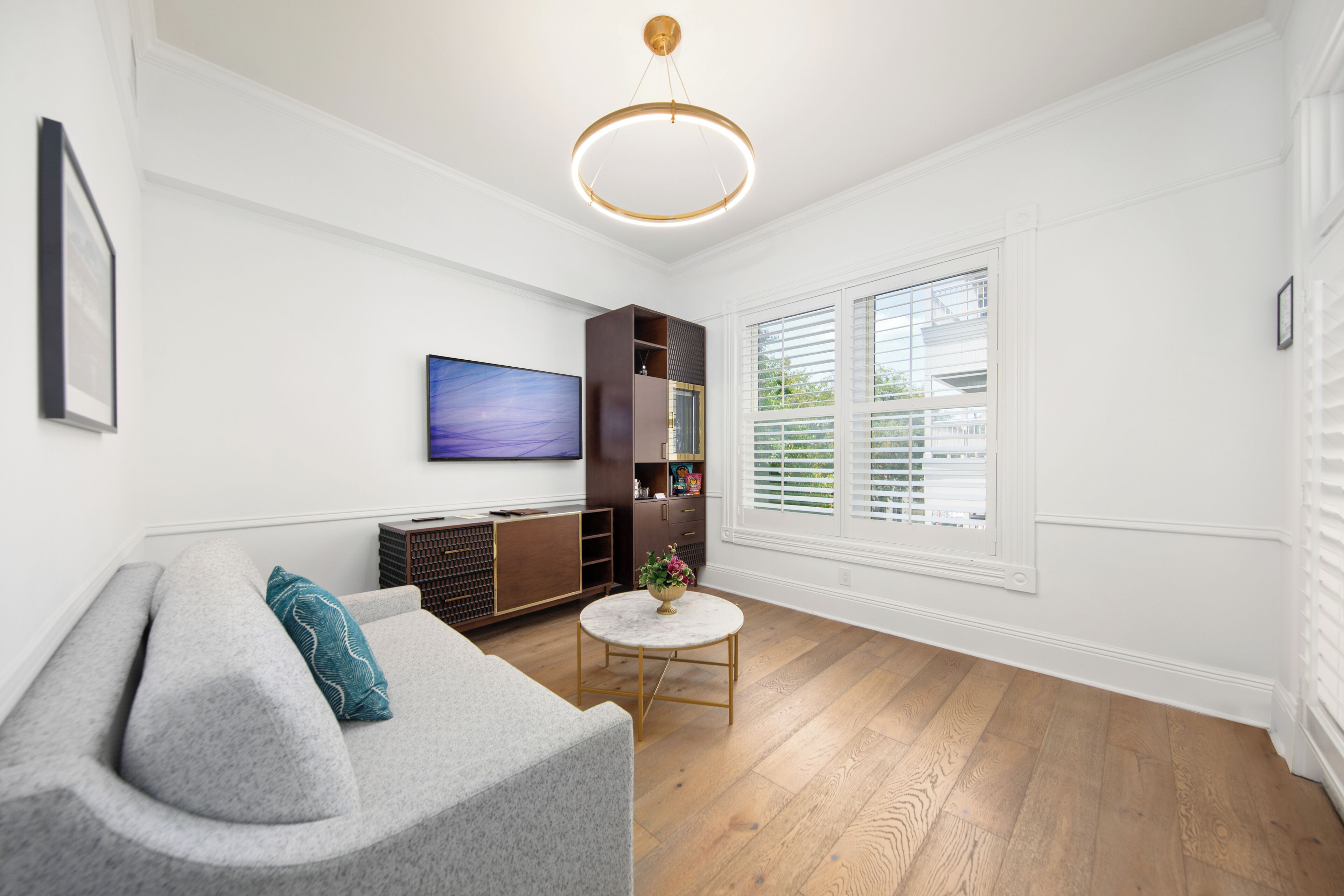 A modern living room with a grey sofa, a round coffee table, and a flat-screen TV mounted on the wall.