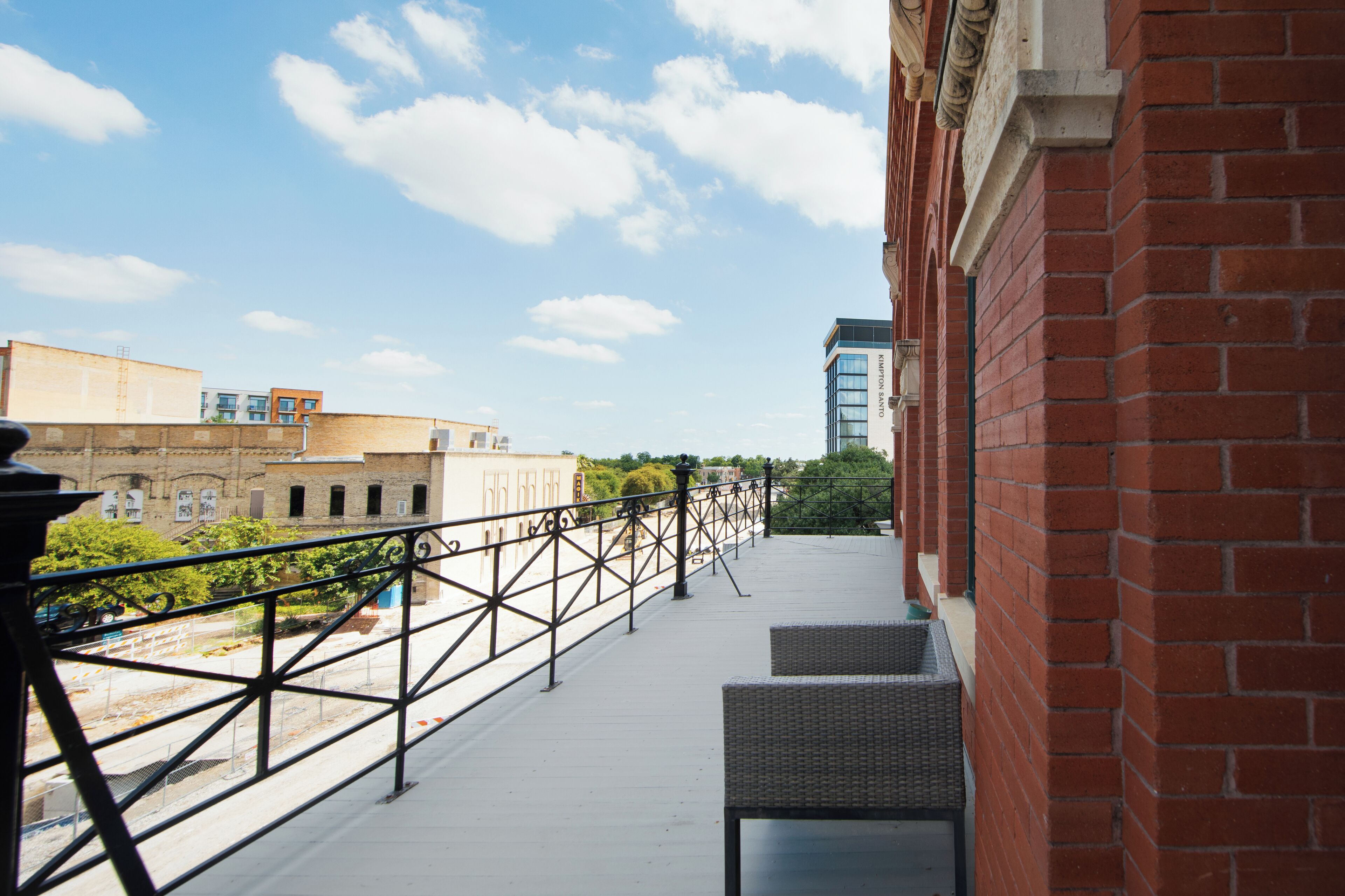 Un balcon avec des fauteuils en osier, une rambarde en métal et une vue sur des immeubles et des arbres.