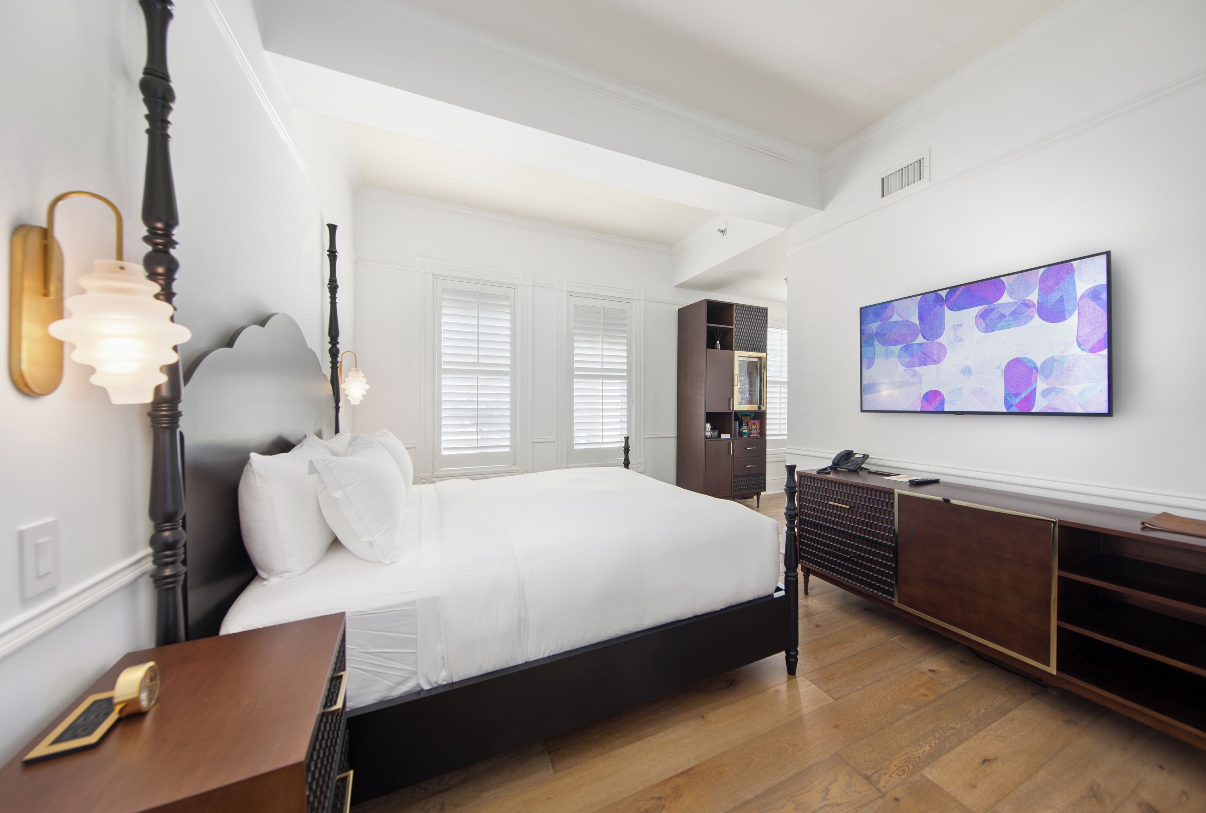 A bedroom with a large bed, a dresser, a nightstand, and a wall-mounted TV.