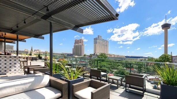 A rooftop terrace with wicker furniture, potted plants, and a clear view of city buildings and a tower. - Fairmount Hotel (San Antonio)