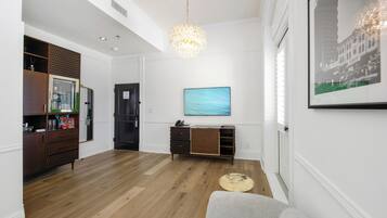 A modern living room with hardwood flooring, a grey sofa, a wooden cabinet, a television, and a chandelier.