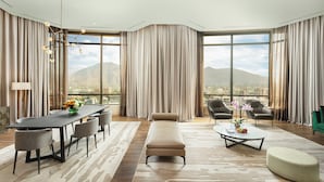 Una habitación de hotel moderna con un ventanal grande, un área de comedor, un sofá y una mesita de centro.