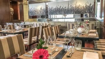 A restaurant with striped upholstered chairs, neatly set dining tables with wine glasses, and a large mirror reflecting the room.