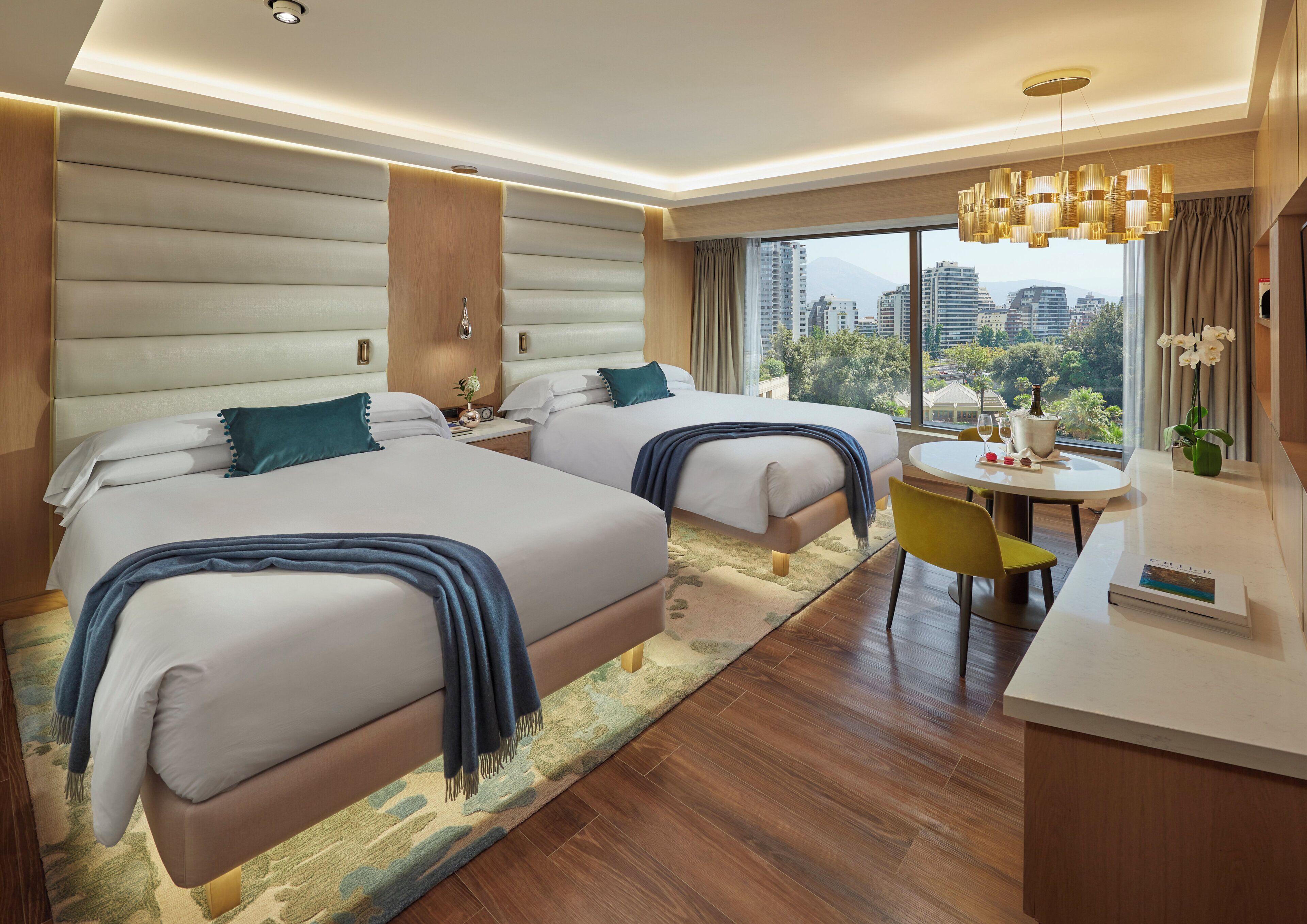 Habitación de hotel con dos camas, zona de comedor y vistas a la ciudad.