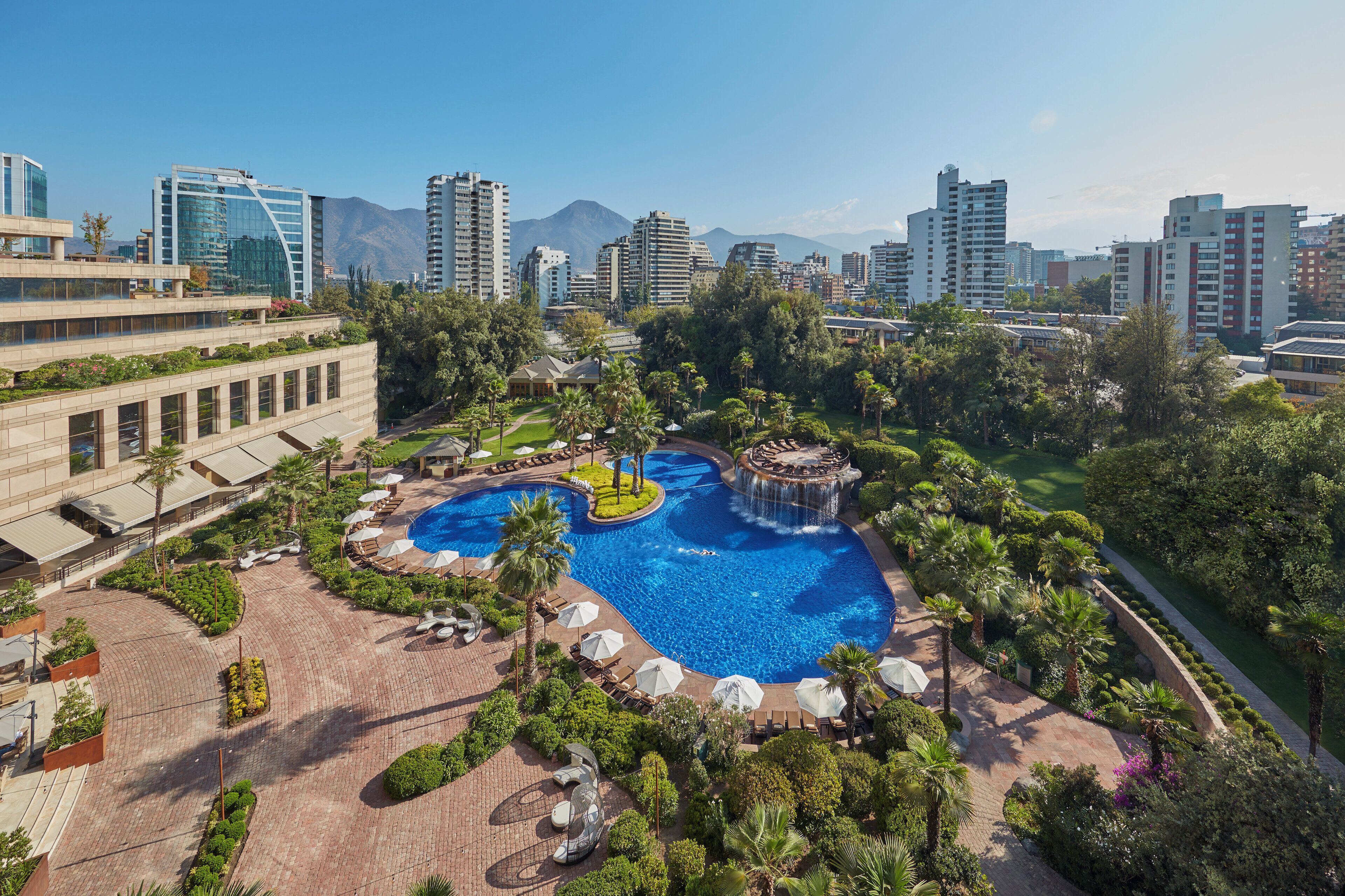 A resort with a central swimming pool, lounge areas, and a mountainous backdrop.