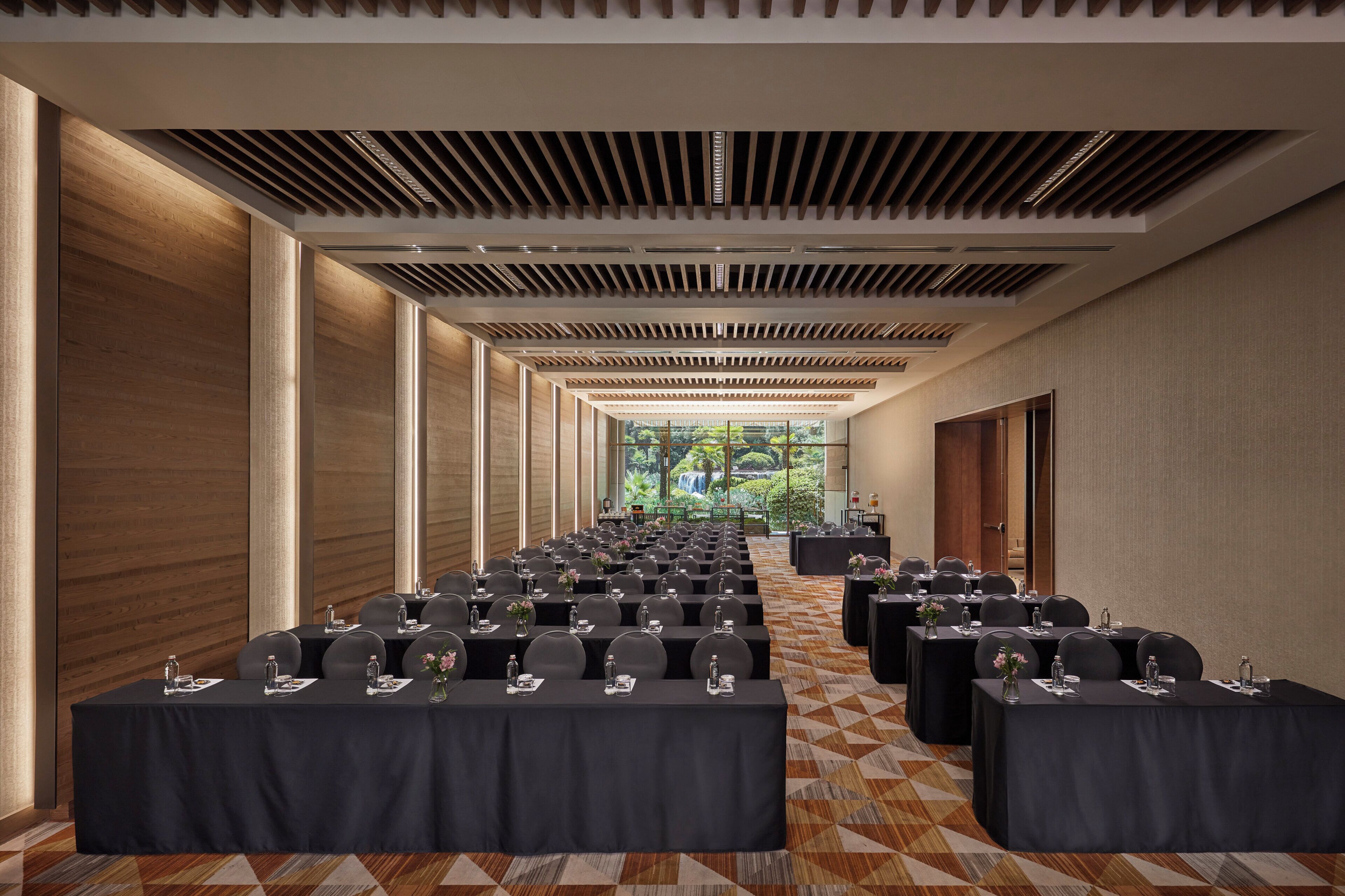 A conference room with rows of tables, chairs, and a view of a waterfall through large windows.