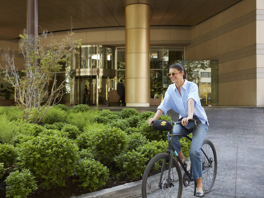 A person riding a bicycle in front of a building with a glass entrance and a well-maintained garden area.