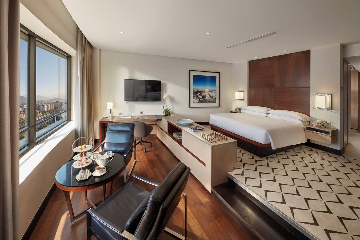 A hotel room with a bed, desk, chair, and a table with a tea set.