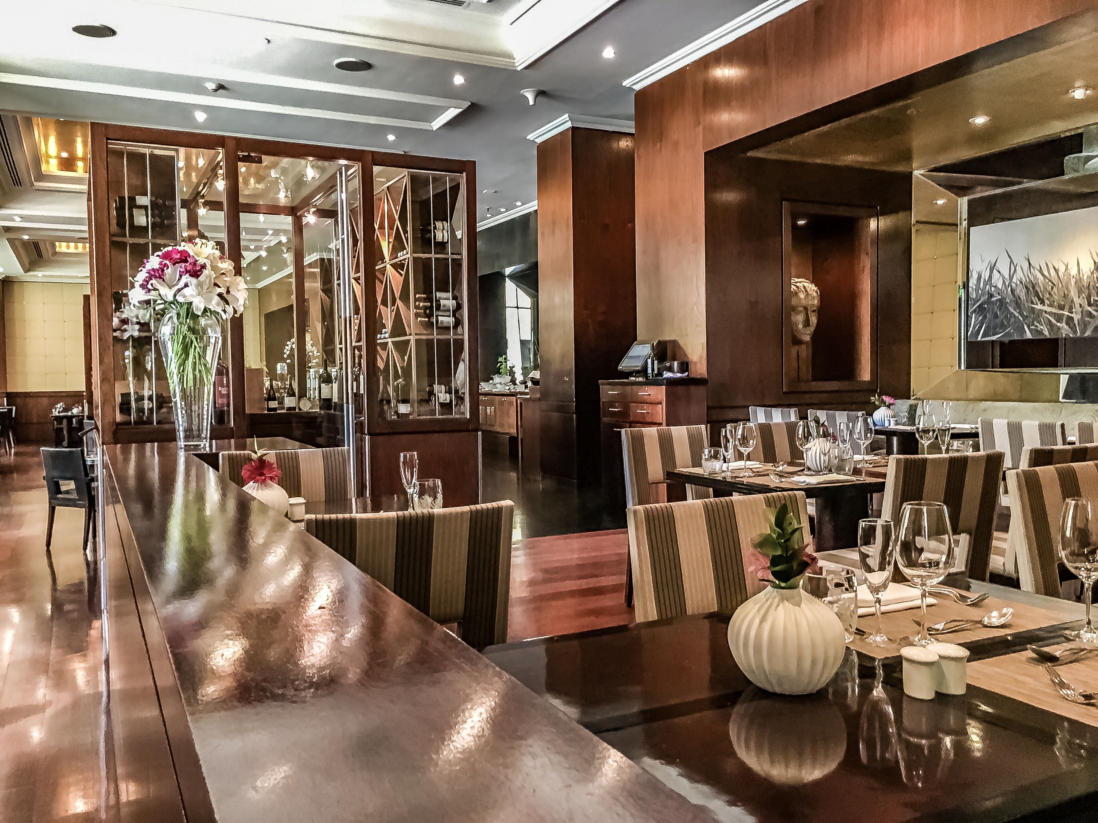 Un restaurante con una barra larga, sillas a rayas y un jarrón grande con flores.