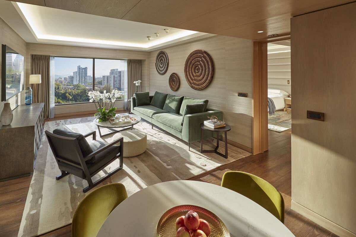 A modern living room with a sofa, coffee table, and chairs. There is a large window with a city view.