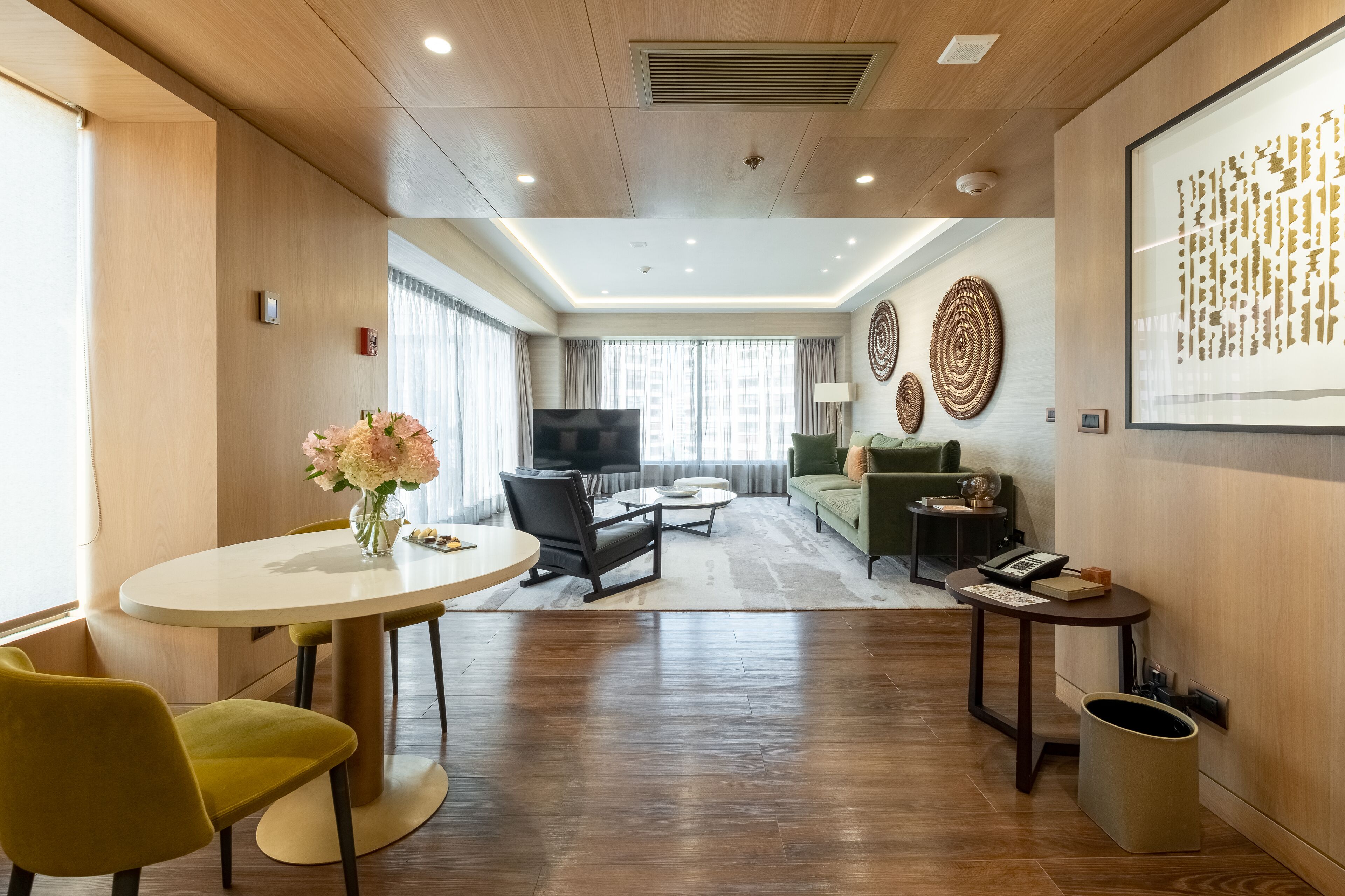 Een moderne woonkamer met een ronde eettafel, gele stoelen, een bank, een televisie en decoratieve wandkunst.