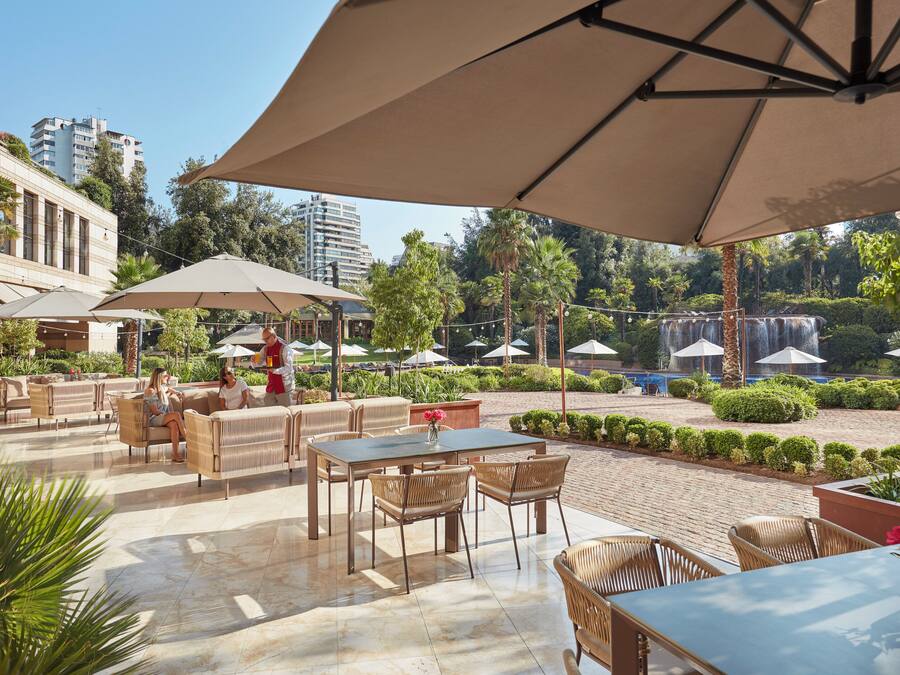 An outdoor patio area with tables and chairs, umbrellas, and a fountain in the background.
