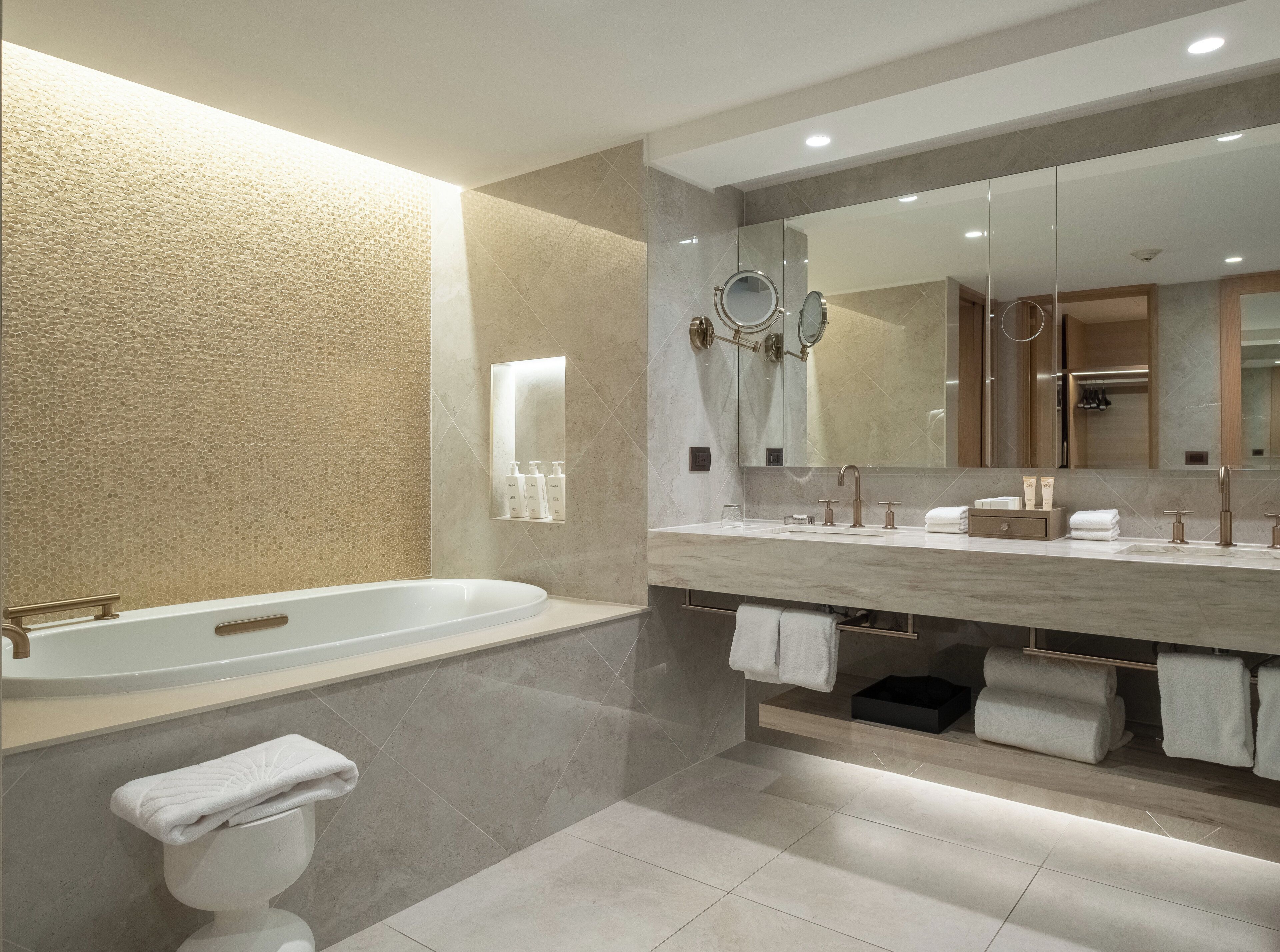A modern bathroom with a bathtub, a large mirror, and a vanity with toiletries.