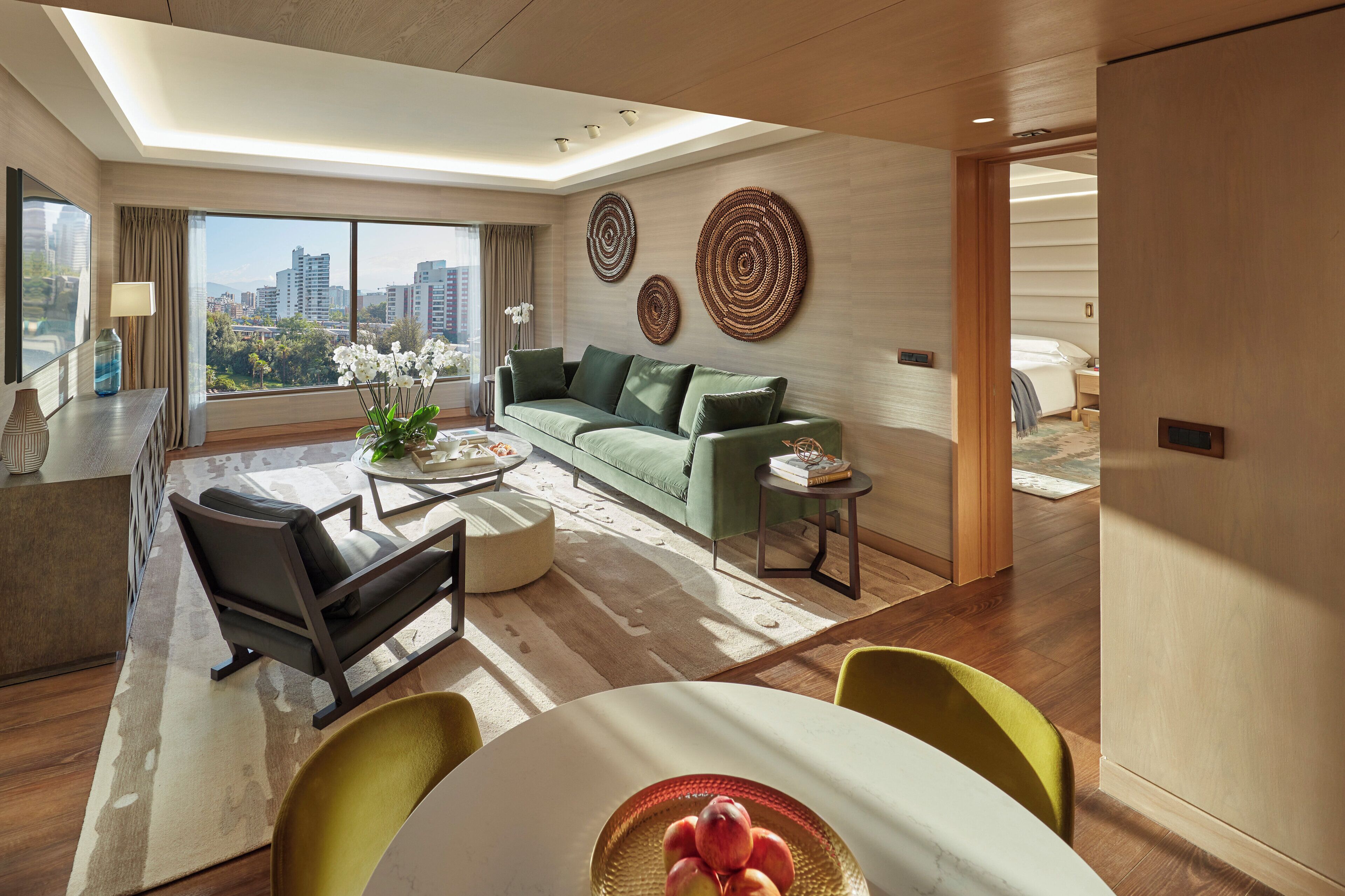 A modern living room with a sofa, coffee table, and chairs, a dining area with a table and chairs, and a view of a cityscape through large windows.