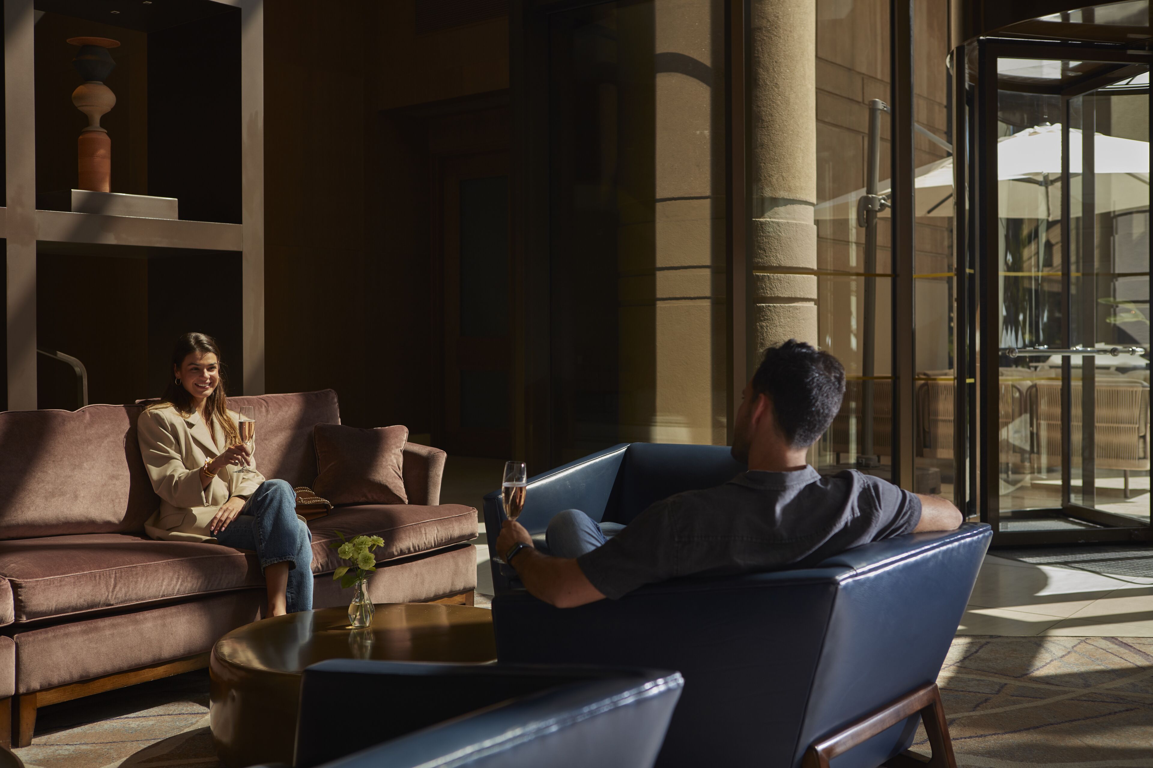 A modern lobby with leather sofas, a coffee table, and a glass door leading outside.