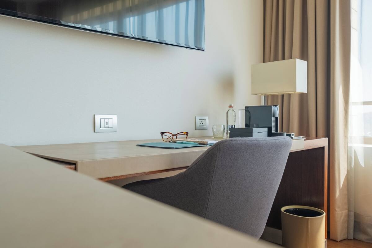 Una habitación de hotel con cama, escritorio con lámpara, televisión y ventana con cortinas.