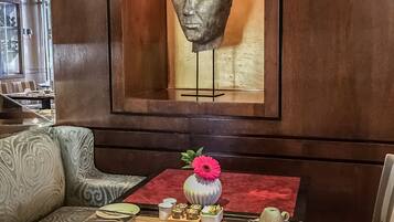 Un coin repas avec une table dressée pour deux personnes, un vase avec une fleur et une sculpture en buste accrochée au mur.