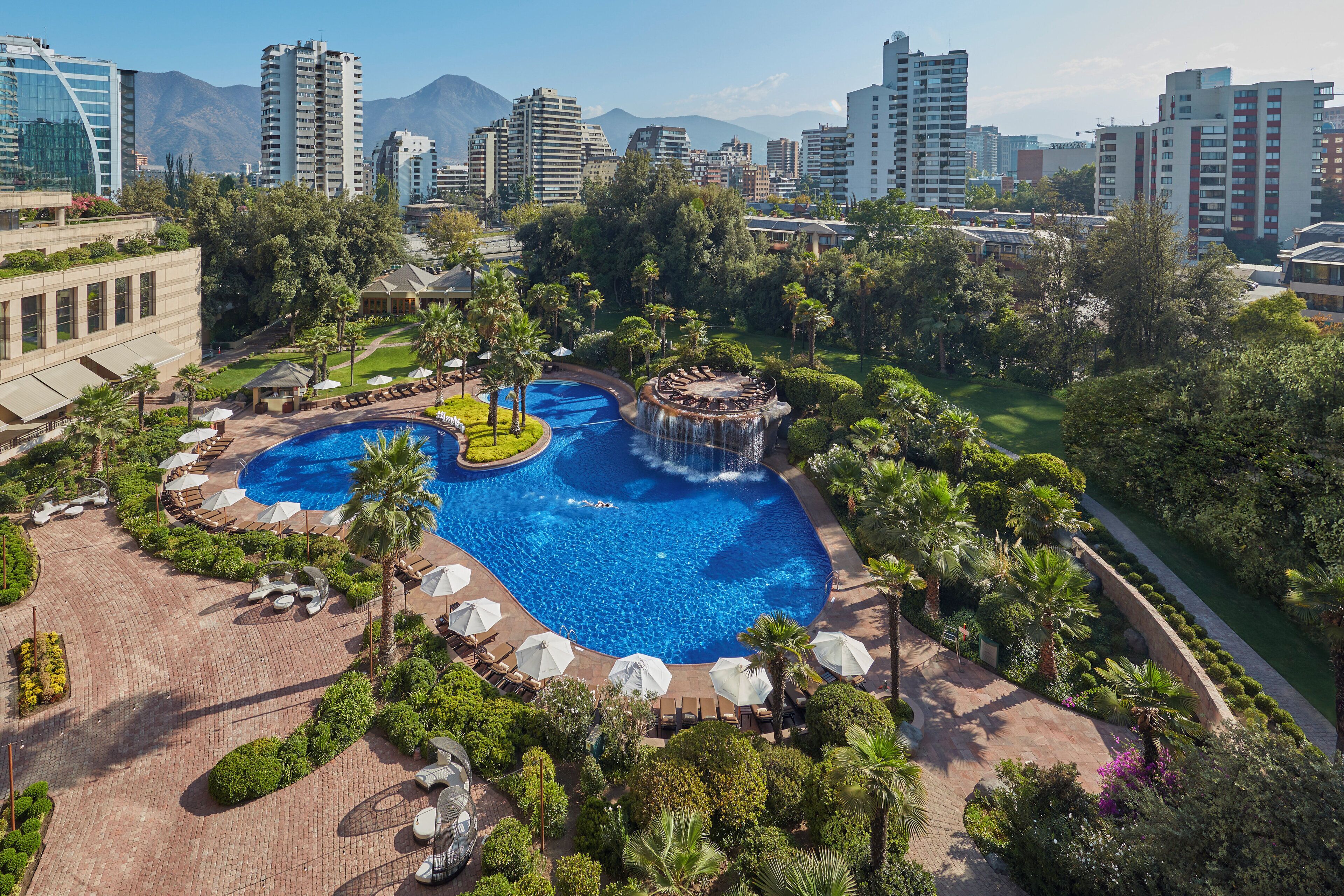 A resort with a large pool, palm trees, and a cityscape in the background.