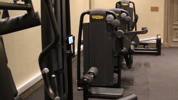 A gym with various exercise machines, a wall-mounted television, and a door in the background.