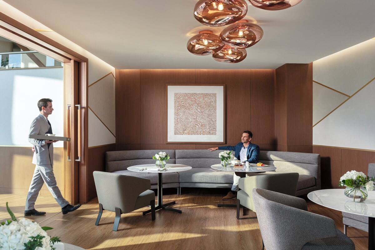 A modern hotel lobby with a curved grey sofa, round tables, and a large abstract artwork on the wall.