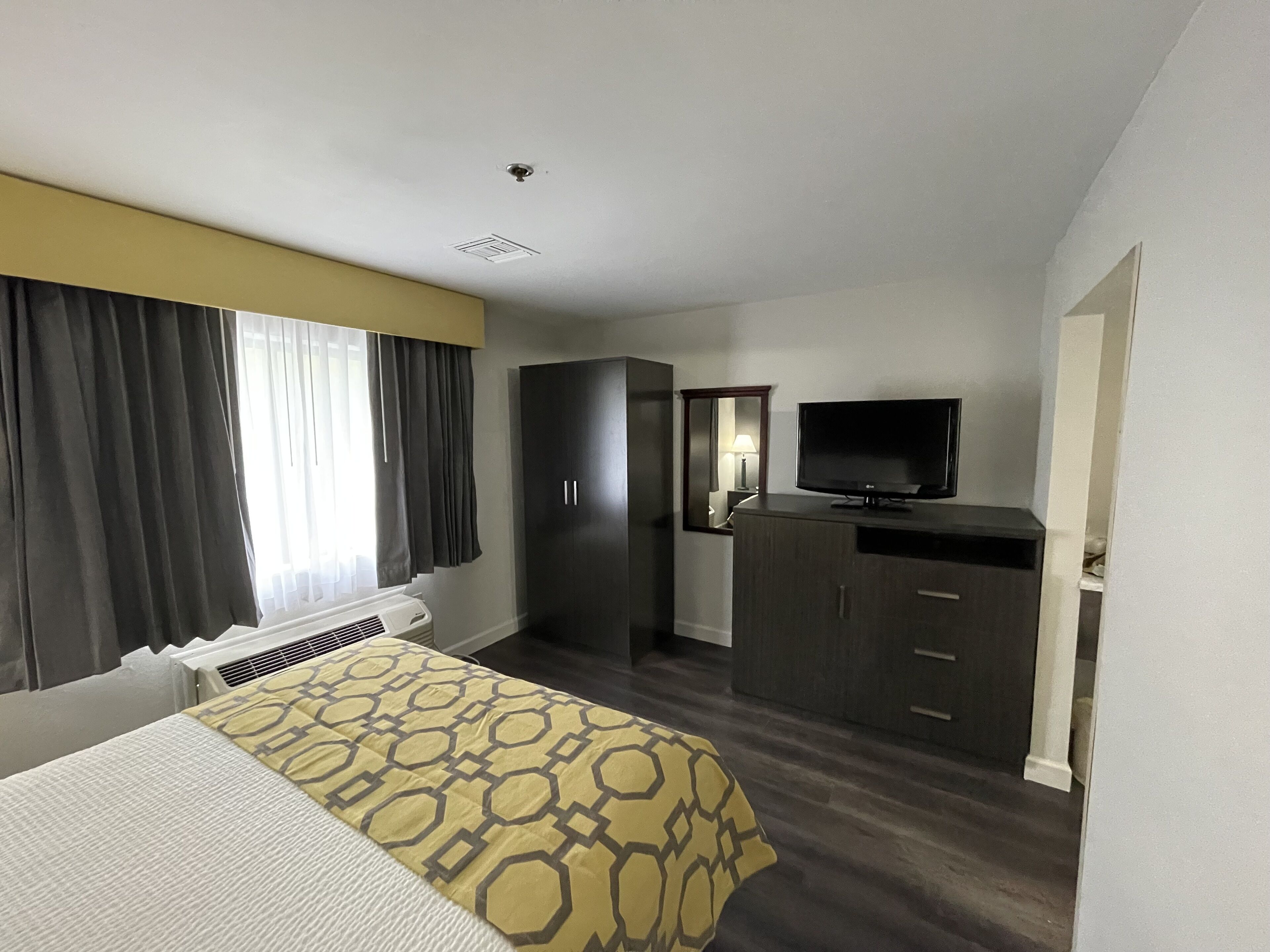 A hotel room with a bed, a television, a wardrobe, and a mirror.