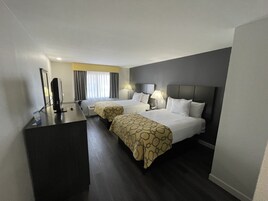 Quarto de hotel com duas camas, uma escrivaninha, um computador e uma janela com cortinas.