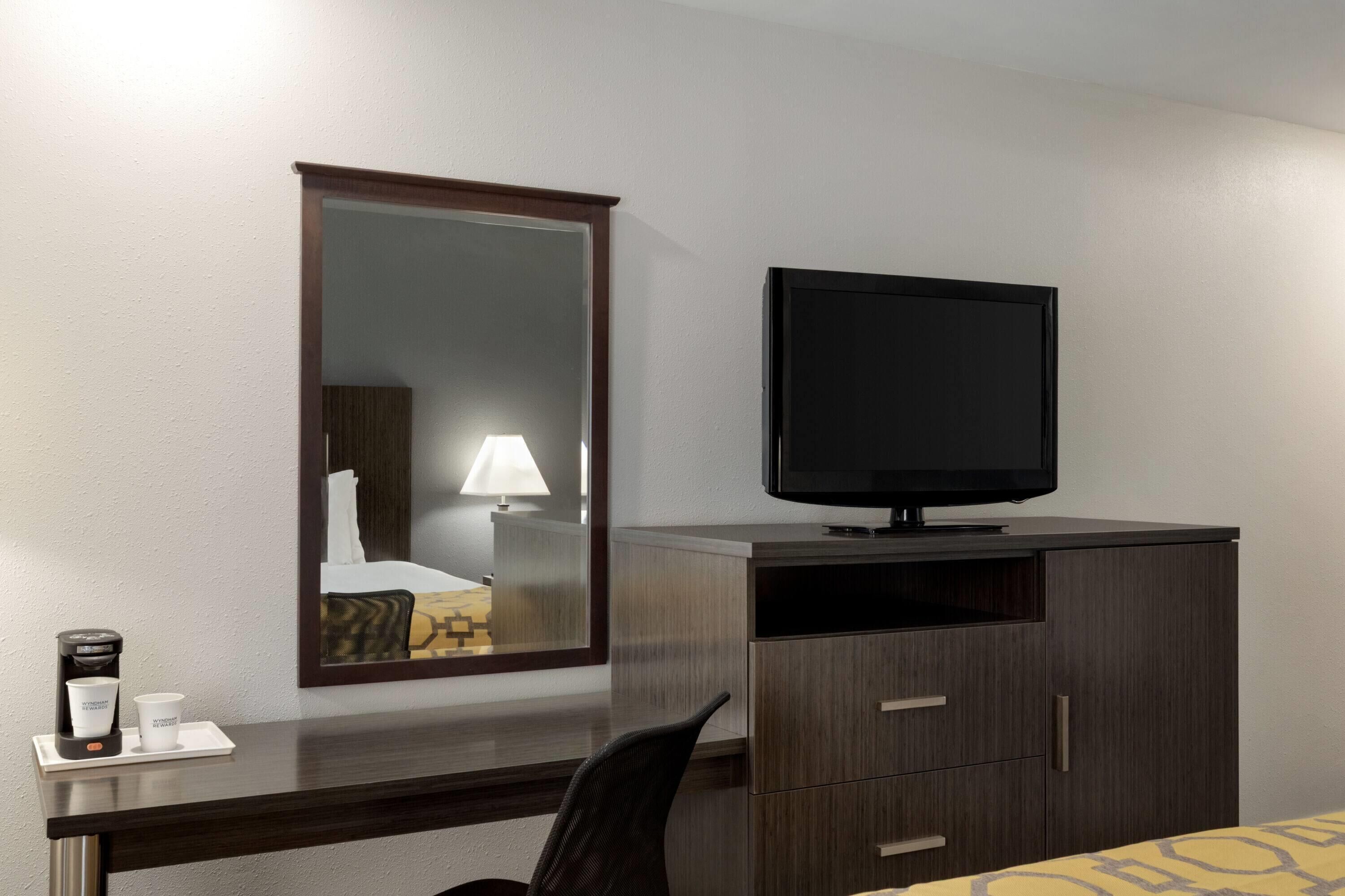 Habitación de hotel con un escritorio de madera oscura, televisor, espejo y cama con una colcha amarilla estampada.